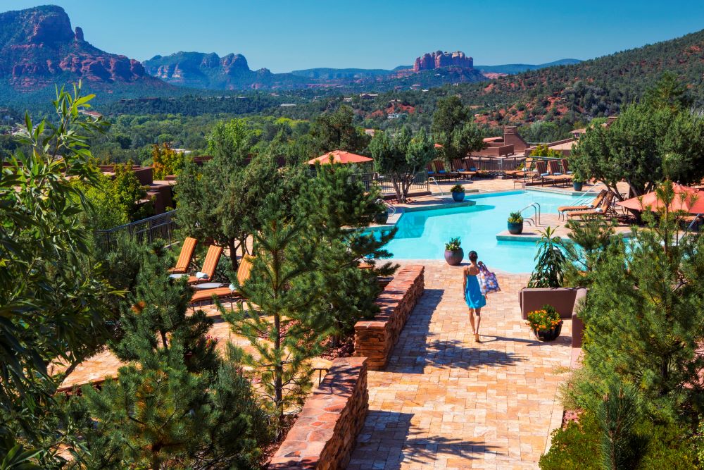 A woman carries a stylish tote bag toward a swimming pool at Hyatt Vacation Club Sedona, Piñon Pointe, with a specatcular view of natural Arizona in the background.