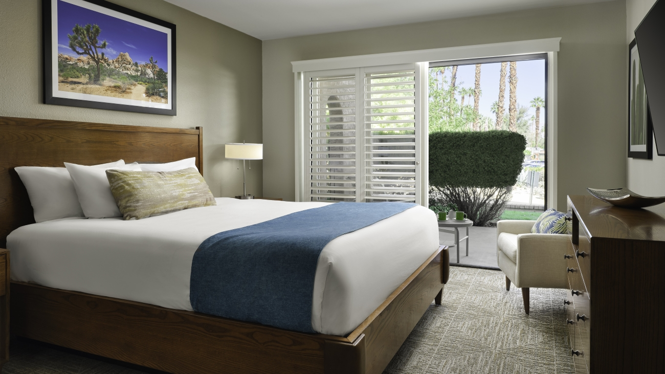 Inside view of a villa bedroom with bed, armchair, dresser, and colorful framed art on the wall