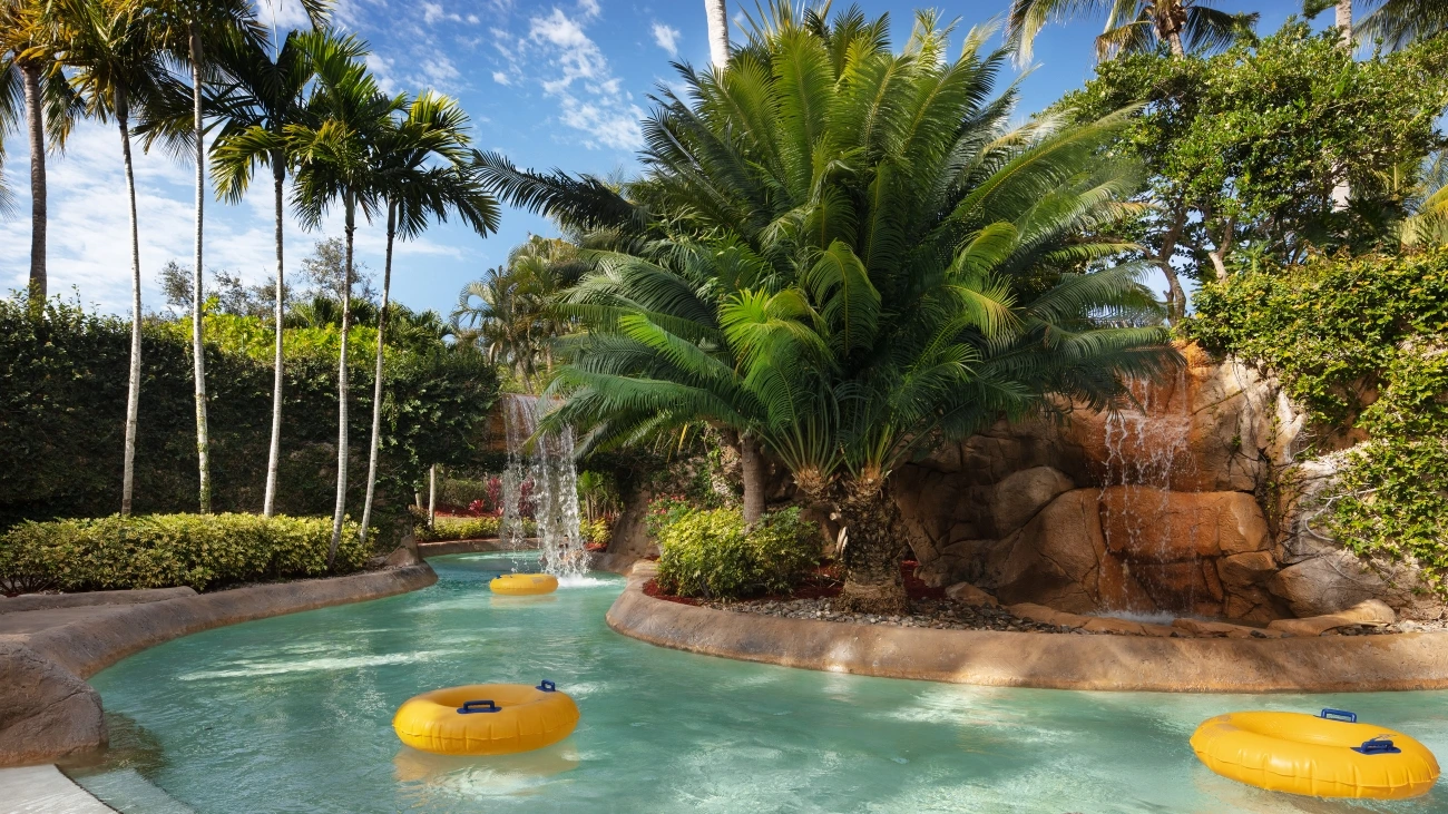 Yellow innertubes float down a lazy river featuring a weaterfall and plenty of green trees