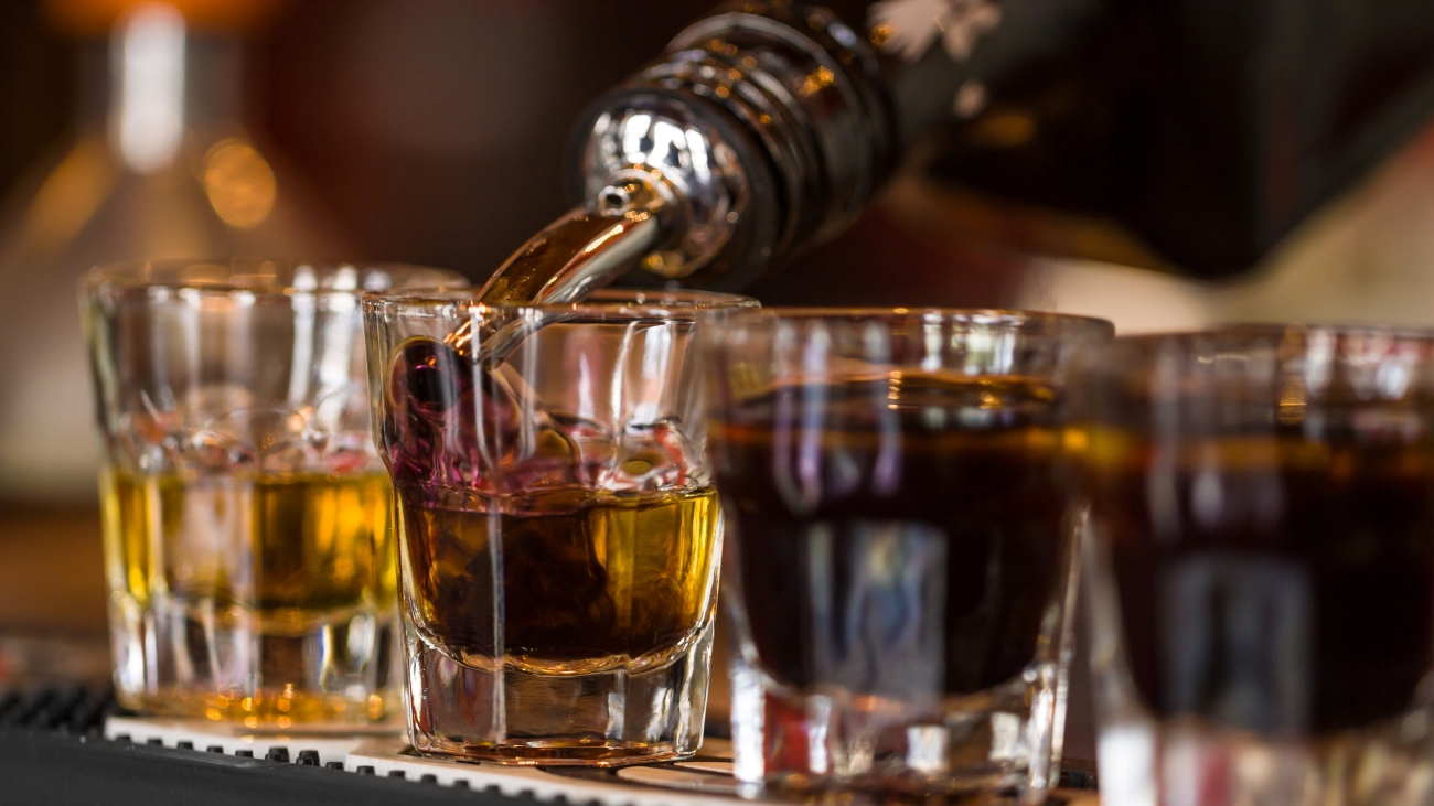 Rum being poured into shot glasses on a bar