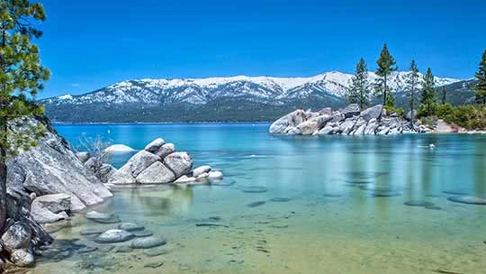 Crystal-clear lake waters with beautiful rocky shore and snow-capped mountains in background