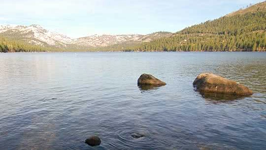 Peaceful waters of Lake Tahoe with rocks emerging from the water and pine-tree covered hills in background