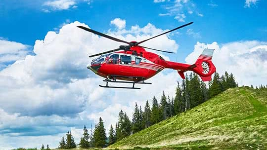 Red and white helicopter flying over an alpine landscape on a bright sunny day