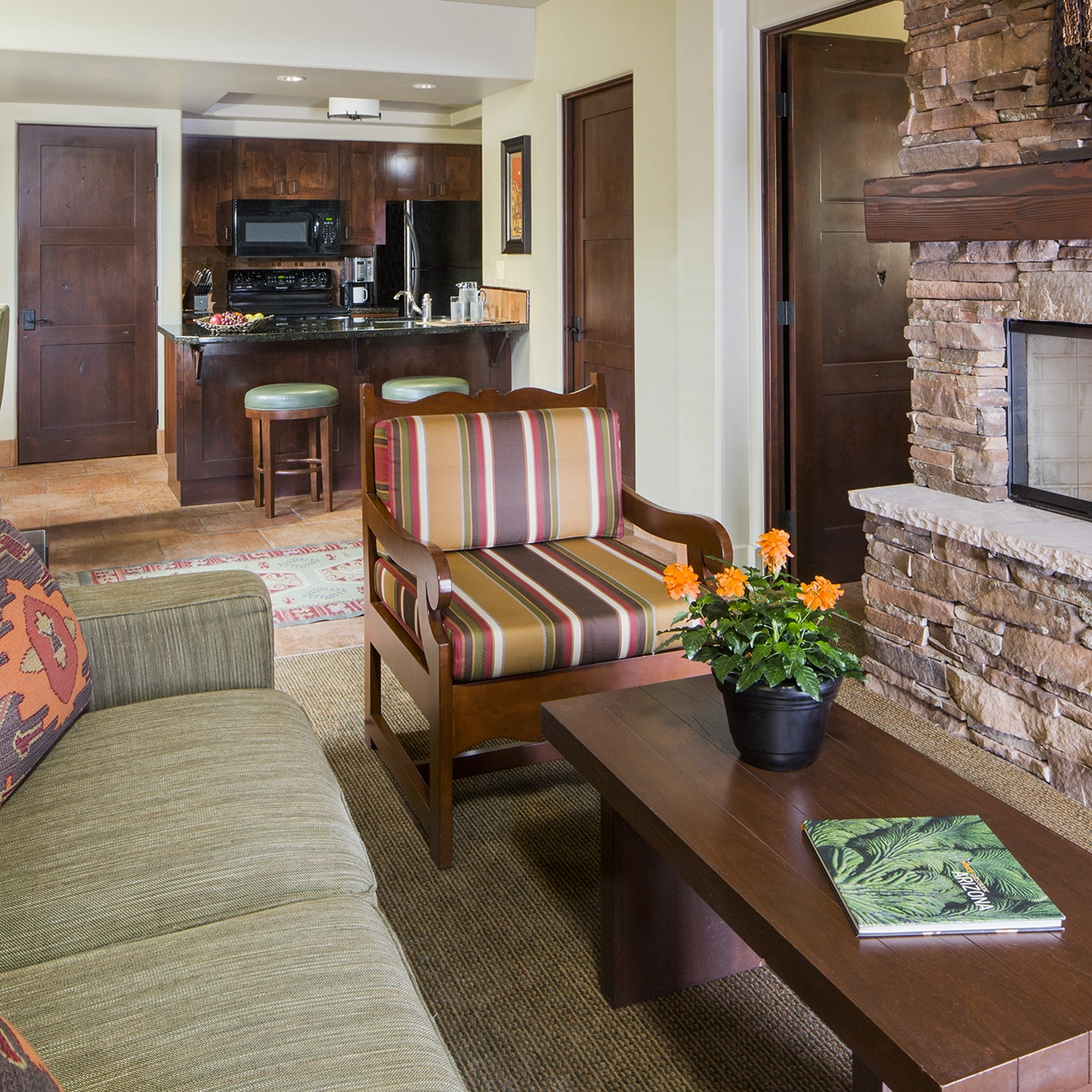 A couch and chair sit in a living area of a villa in front of the fully equipped kitchen